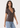 A woman modeling a short-sleeve brown V-neck t-shirt paired with light blue jeans, photographed against a clean white studio background.