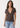 A woman modeling a short-sleeve brown V-neck t-shirt with a wrap-style front, paired with light-wash blue jeans, against a plain off-white studio background.