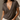A woman wearing a dark brown short-sleeve V-neck t-shirt and off-white jeans, standing against a textured beige wall with warm sunlight and shadows.