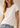 A woman wearing a short-sleeve crew-neck t-shirt in off-white, paired with light-wash blue jeans, shown from the waist up against a neutral beige background.