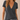 A woman wearing a dark charcoal gray short-sleeve V-neck t-shirt and light blue jeans, shown from the neck down against a neutral beige background.
